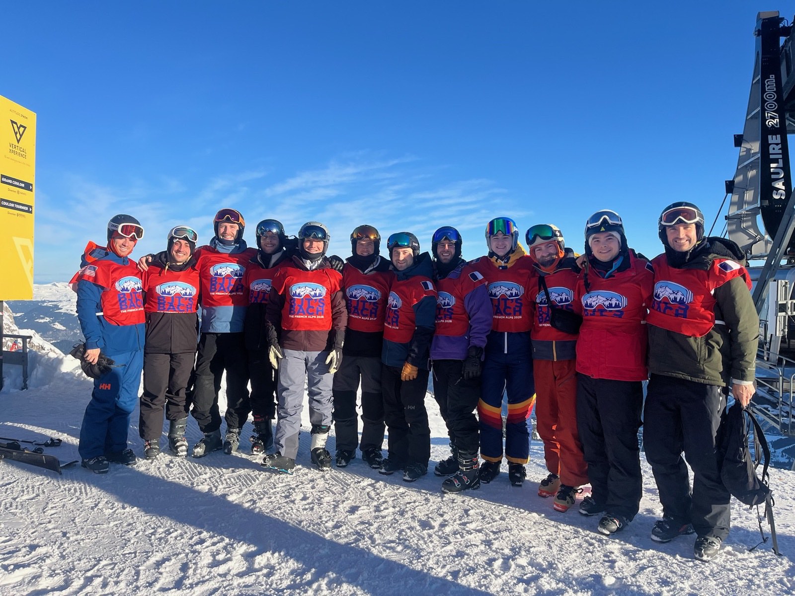 Group of skiers in matching red sublimated group bibs at the top of a French Alps lift